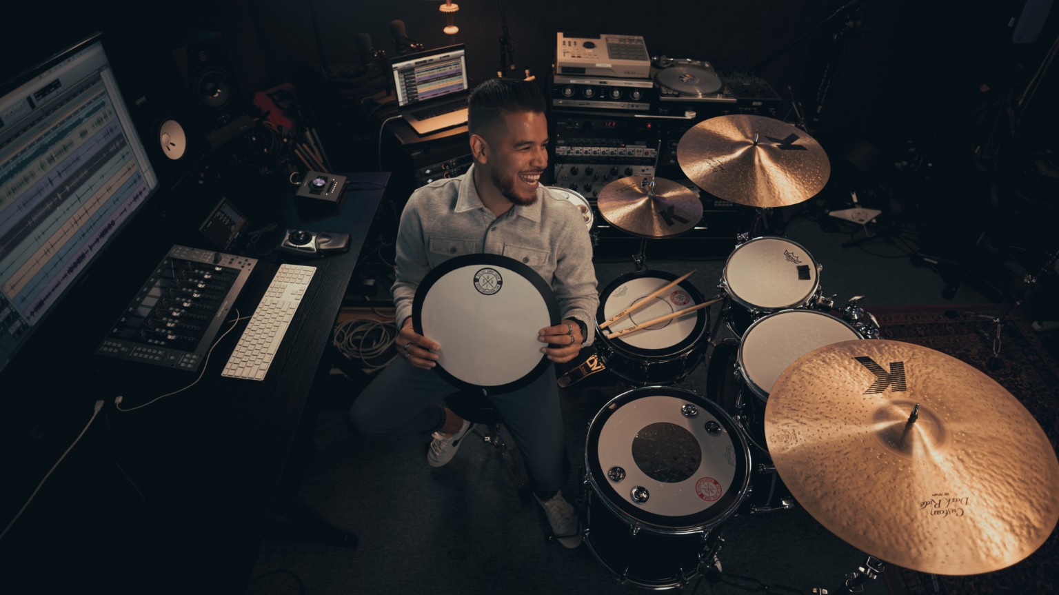 Kevin Michael Chong holding a Big Fat Snare Drum accessory above his drum kit